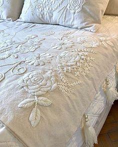 a bed with white linens and embroidered flowers on the comforter, along with two pillows