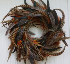 a wreath made out of feathers hanging on the side of a white door with an orange and black design