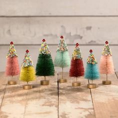 small christmas trees with colorful pom poms on them are lined up against a wooden table