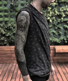 a man with tattoos on his arm and shoulder standing in front of a wooden deck