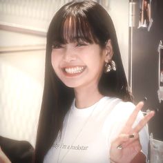 a woman with long black hair smiling and giving the peace sign in front of her