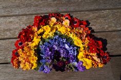 a bunch of flowers that are on top of a wooden table and in the shape of a rainbow