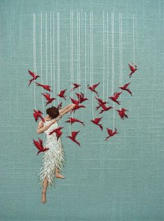 a woman is surrounded by red birds hanging from strings on a blue background with white thread