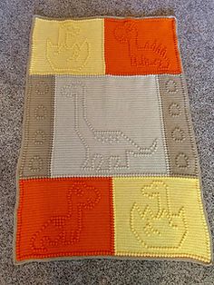 a crocheted blanket with an orange, yellow and gray design on it's side