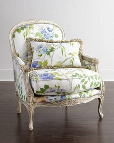 an ornate chair with blue flowers and green leaves on the back, against a white wall