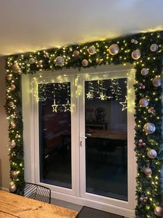 a room with christmas lights and decorations on the wall, windows open to let in light