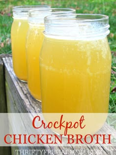 three mason jars filled with chicken broth sitting on top of a wooden bench in the grass