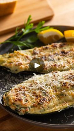 two fish fillets on a black plate with lemons and parmesan cheese