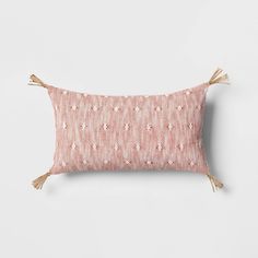 a pink and white pillow with tassels on the front, sitting against a wall