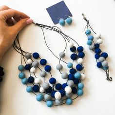 two necklaces made out of felt balls being held by someone's hand over a white table