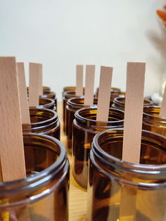 several mason jars with wooden sticks sticking out of the top, lined up on a table