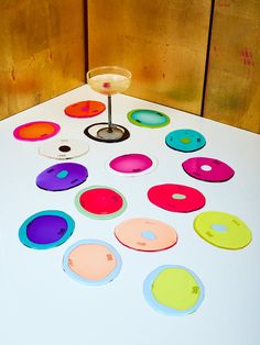 a white table topped with lots of different colored plates and a wine glass on top of it