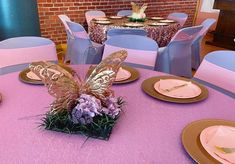 the table is set with pink and gold plates, napkins, and butterfly centerpieces