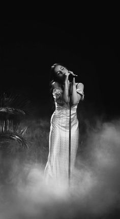 a black and white photo of a woman in a dress singing into a microphone on stage