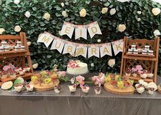 a table topped with cakes and cupcakes next to a wall covered in greenery