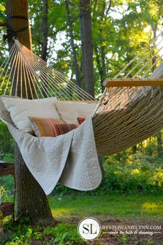 a hammock hanging in the middle of a forest with pillows and blankets on it