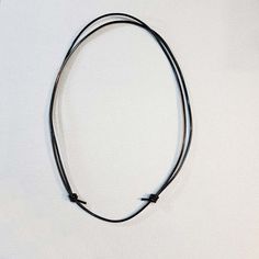 a black leather necklace with two silver beads on it's end and a cord attached to the clasp