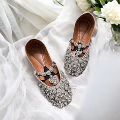 two pairs of shoes are sitting on a white cloth with flowers in the vase behind them