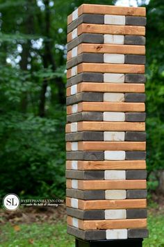 a sculpture made out of wooden blocks in the grass with trees and bushes behind it