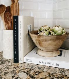 a wooden bowl filled with artichokes sitting on top of a book shelf