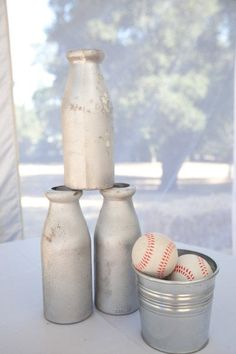 three silver vases with baseballs in them sitting next to a tin can on a table