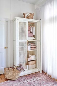 a white cabinet with wicker doors and baskets on the top shelf next to a pink rug