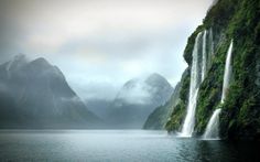 a large waterfall in the middle of a body of water with mountains in the background