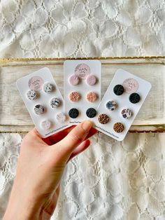 three pairs of buttons are shown in front of a white lace tablecloth, and one is being held by a woman's hand