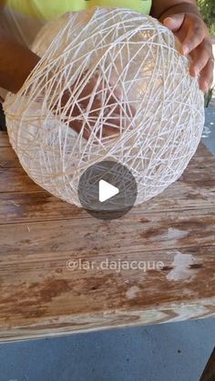 a person is making a sculpture out of yarn on a wooden table with a green shirt