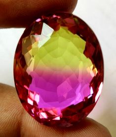 a close up of a person holding a large pink and yellow diamond in their hand