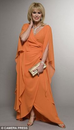 a woman in an orange dress is posing for a photo with her hand on her shoulder