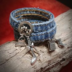 a blue denim bracelet with silver charms and a cross charm on it, sitting on top of a piece of wood