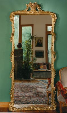 an ornate gold framed mirror in front of a green wall with a painting on it