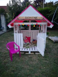 a pink chair sitting in front of a white wooden structure with a sign on it