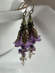 "Rich purple lily blossoms wearing a mantle of vintage-style antique brass caps, cascade a waterfall of tiny natural amethyst. These romantic earrings swing from antique brass French earwires or an earwire of your choice. Leverbacks, kidney wires, posts and non-pierced clips are available.  Please make your selection from the drop-down menu. All Debra Dane jewelry arrives in a pretty box suitable for gifting. 1.5\" (38mm)from bottom loop of earwire." Vintage Floral Jewelry, Whimsigoth Earrings, Cascade Earrings, Plant Earrings, Purple Lily, Amethyst Flower, Purple Accessories, Gift For Gardener, Romantic Earrings