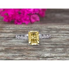 a yellow and white diamond ring on top of a wooden table with pink flowers in the background