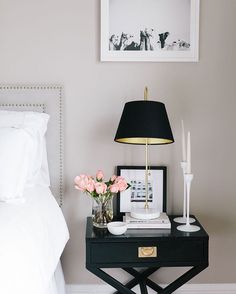 a nightstand with flowers and candles on it next to a framed photograph in a bedroom