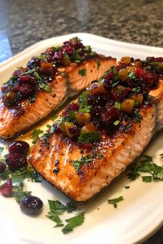 two salmon fillets with cranberry sauce on a white plate next to some garnish