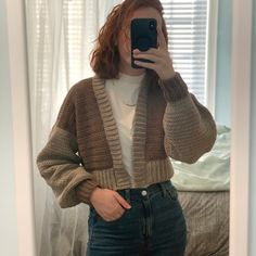 a woman taking a selfie in front of a mirror wearing a sweater and jeans