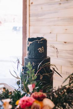 a black wedding cake sitting on top of a table next to flowers and greenery