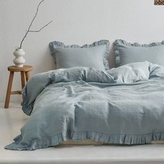 a bed with blue sheets and pillows on top of it in front of a white wall