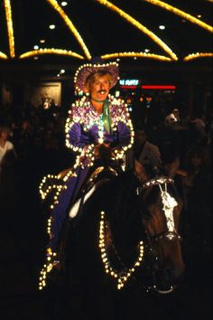 a woman riding on the back of a brown horse in front of a crowd at night