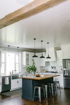 a kitchen with an island and stools next to the counter top in front of two windows