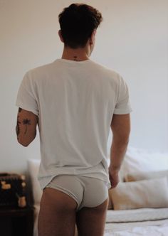 a man in white shirt and shorts standing next to a bed with his back turned