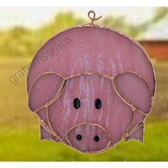 a pink pig hanging from a wire in front of a green grass field and red barn