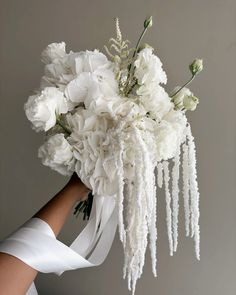 a bouquet of white flowers is held by a woman's hand in front of a gray wall