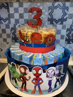 a three tiered cake with spiderman decorations on it's sides and some candy wrapped in plastic wrappers