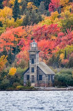 an old building sitting on top of a lake in front of trees with fall colors