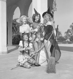 four women dressed up as witches posing for a photo with one holding a broom and the other sitting down