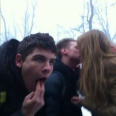 a group of people standing next to each other in the woods eating something out of their mouths